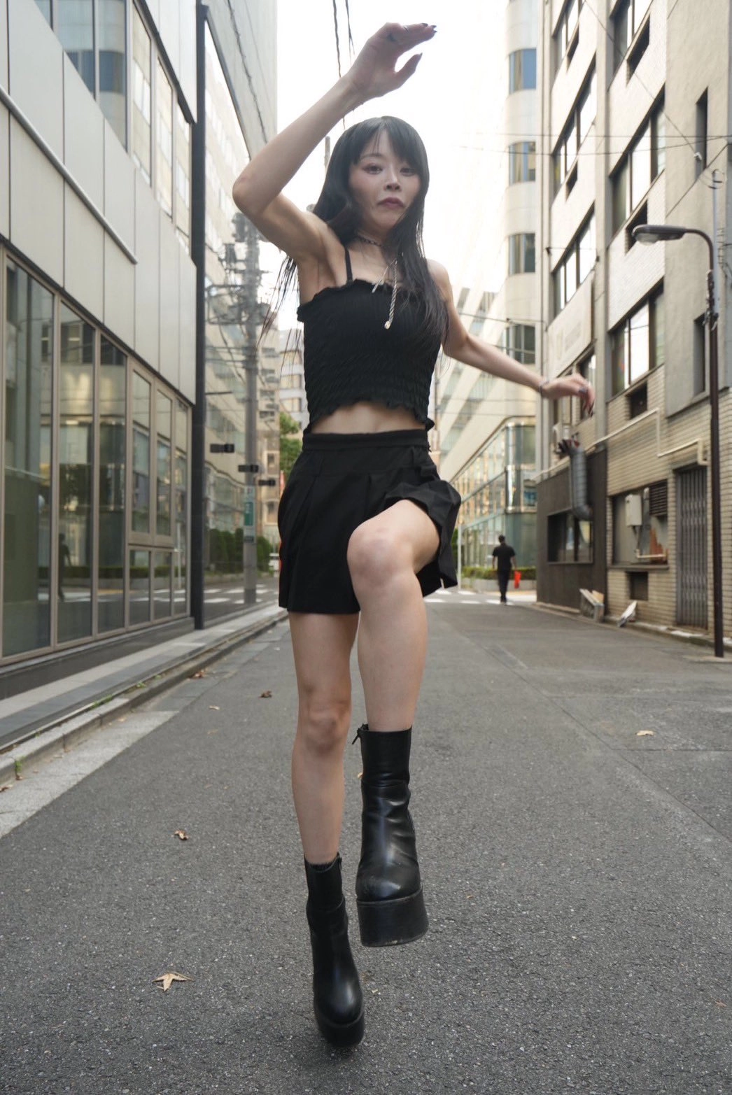 一位穿着黑色短裤和黑靴的女人走在城市街道上。