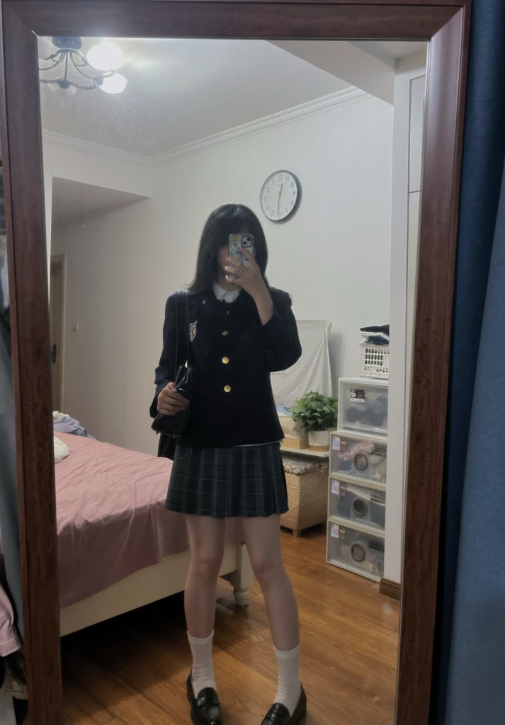 一位穿着黑色外套和裙子的女人在镜子前拍自拍。