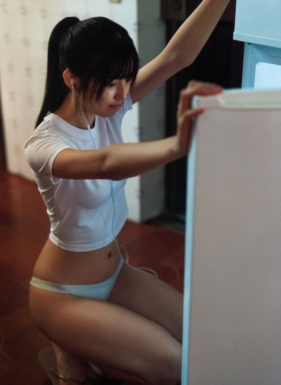 一位穿着白色衬衫和蓝色内衣的女人站在厨房里。