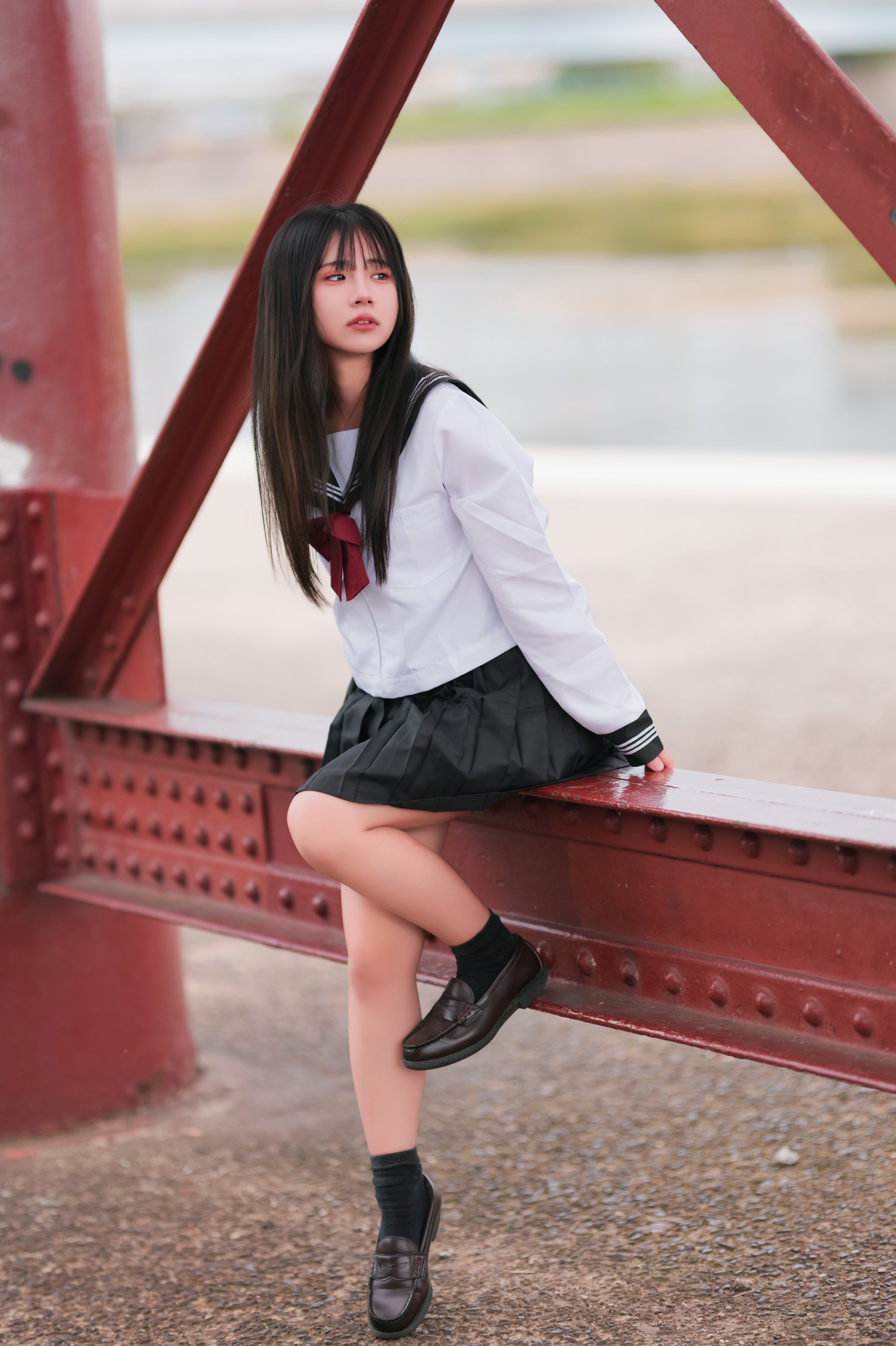 一位穿着白色衬衫和黑色裙子的女孩坐在桥上。