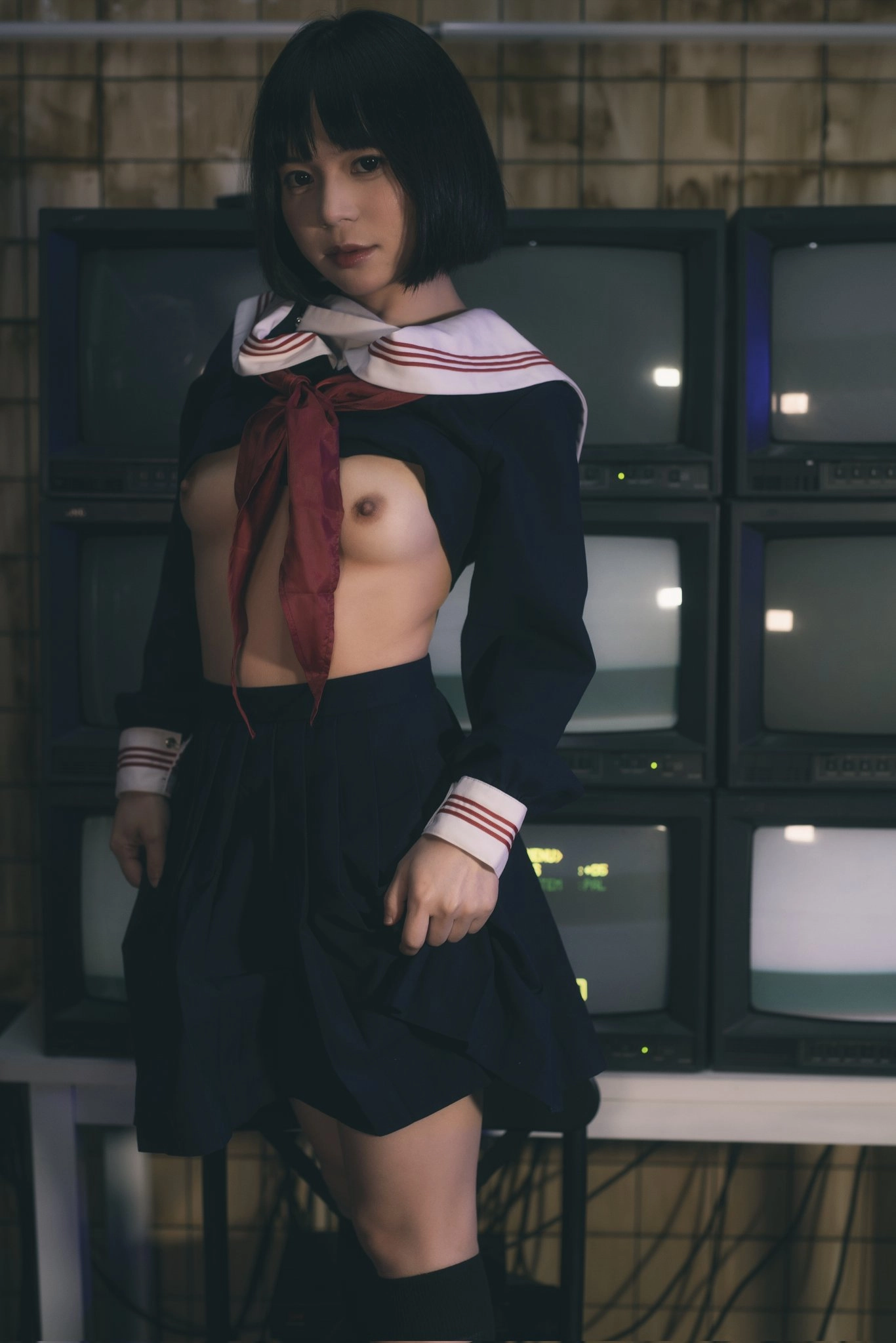 一位穿着女校制服的女子站在一排电视机前。