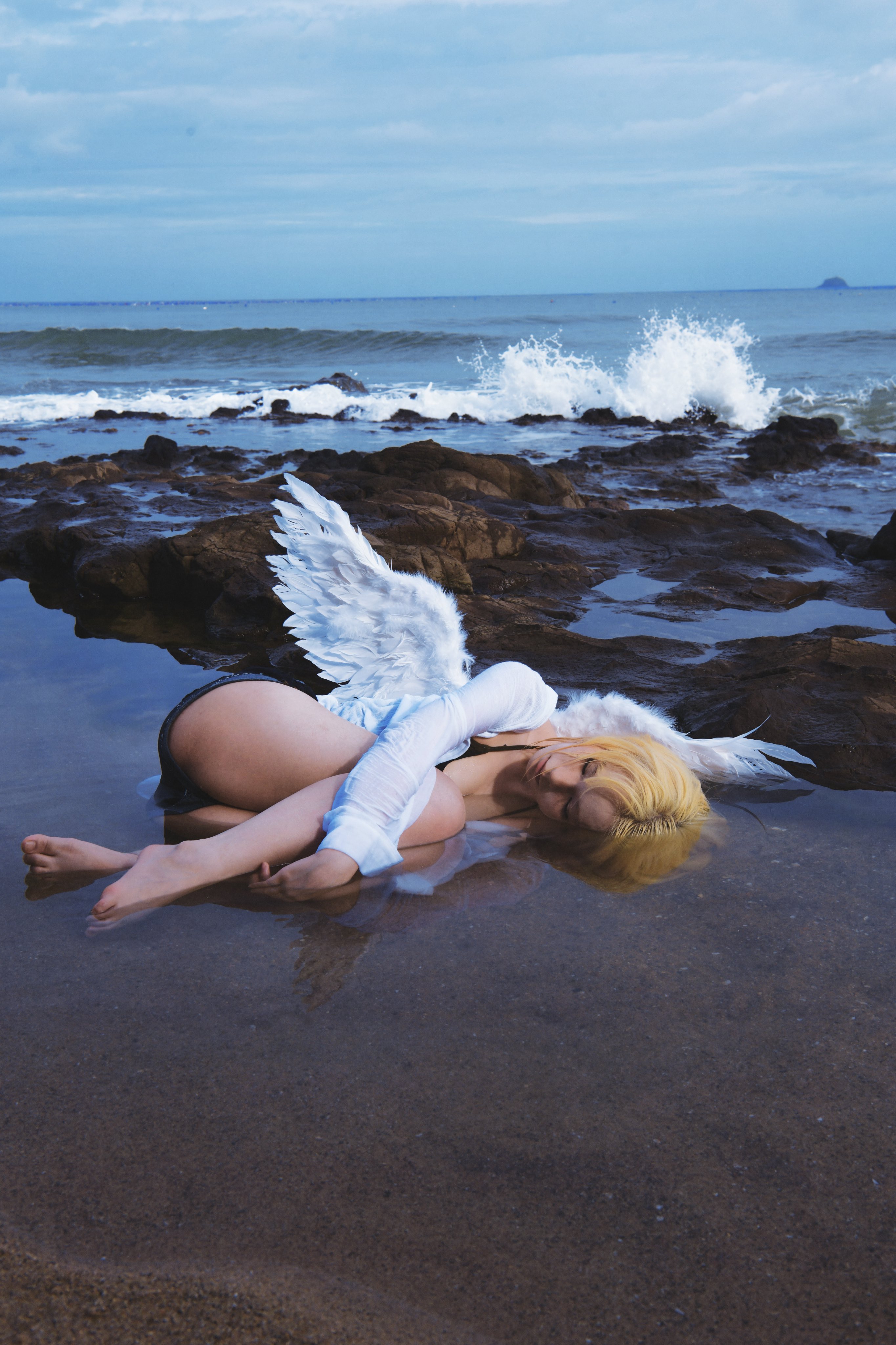 有天使翅膀的女人躺在海滩上。