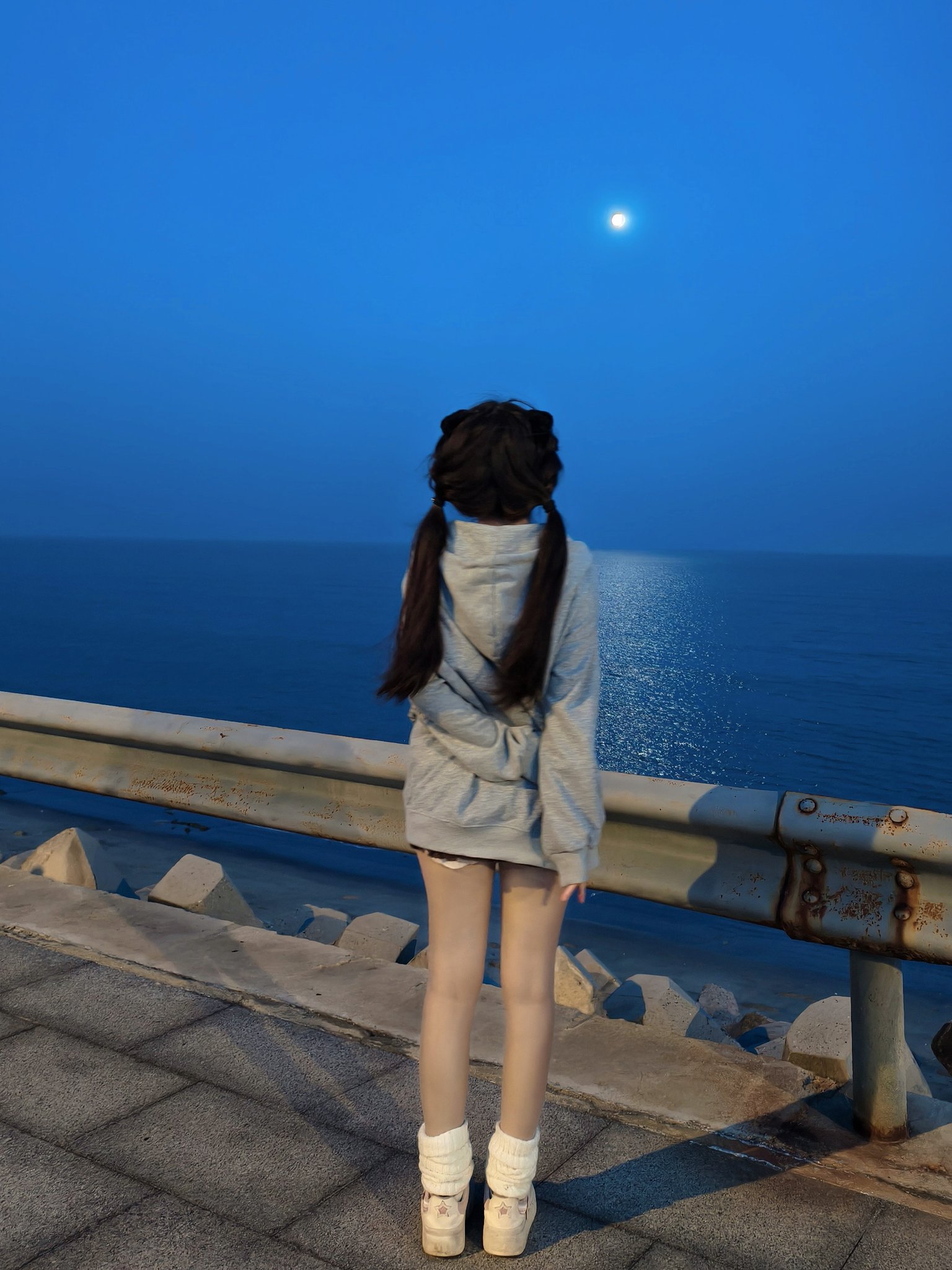 一位穿着帽子的女孩在夜间站在码头上,看着月亮。