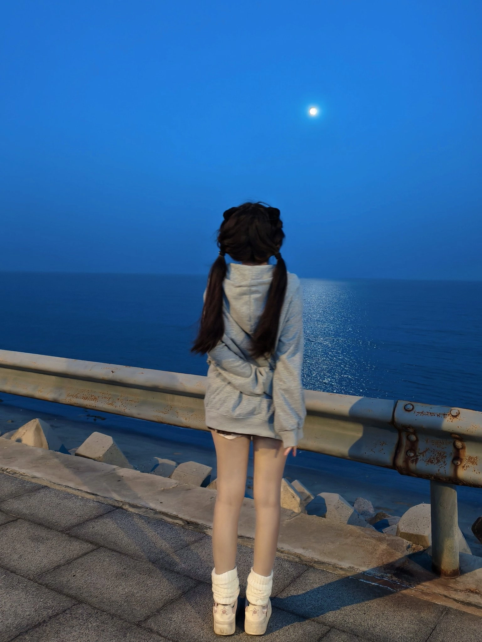 一位穿着帽子的女孩在夜间站在码头上,看着月亮。