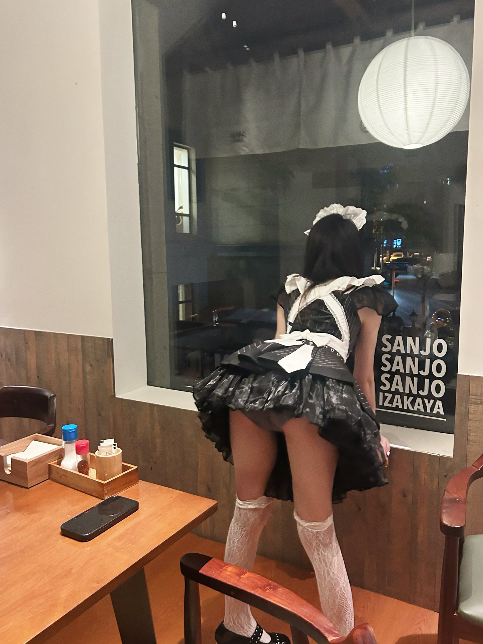 一位穿着女仆的服装的女人站在窗前。