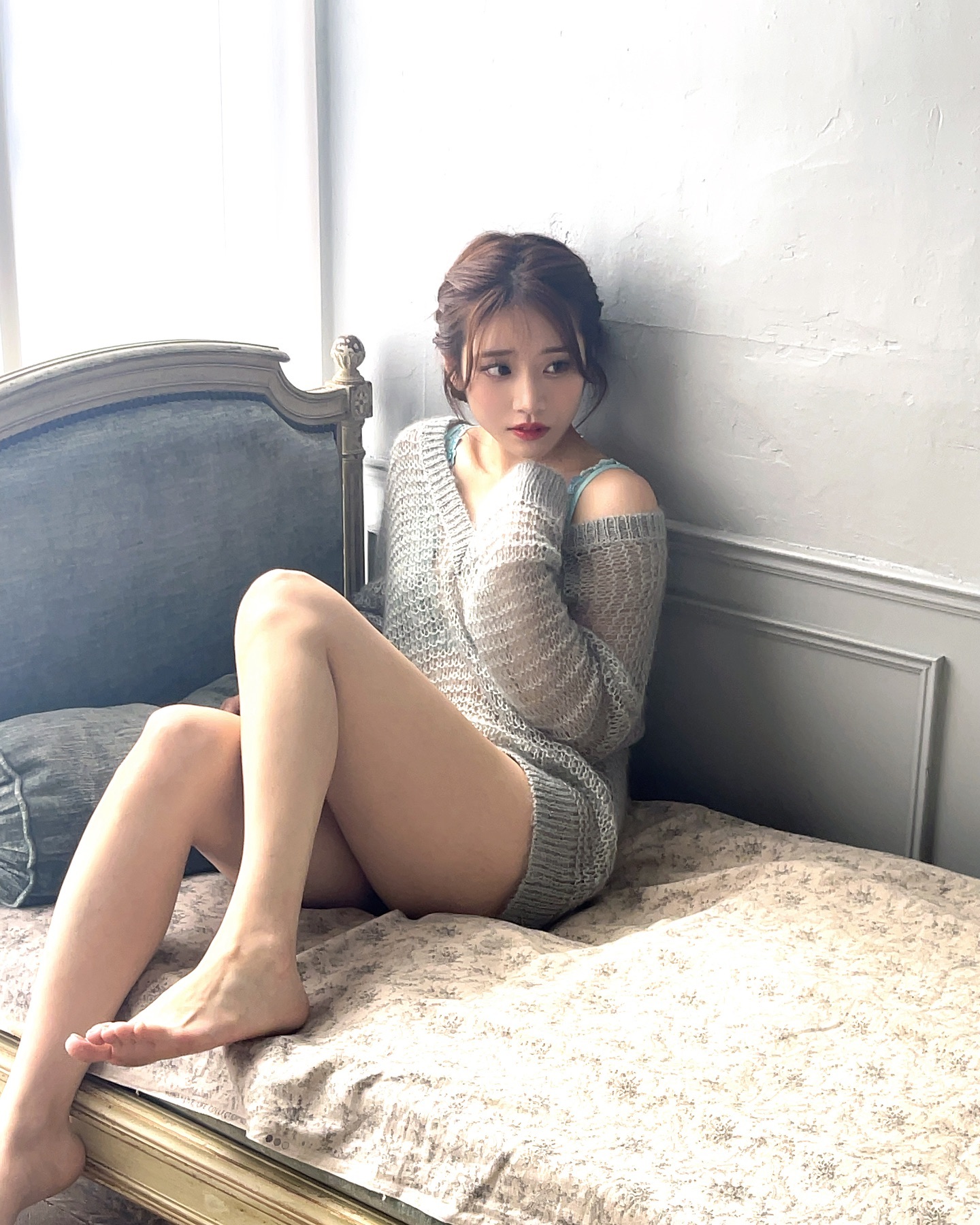 穿着灰色衬衫和蓝色内衣的女人坐在床上。