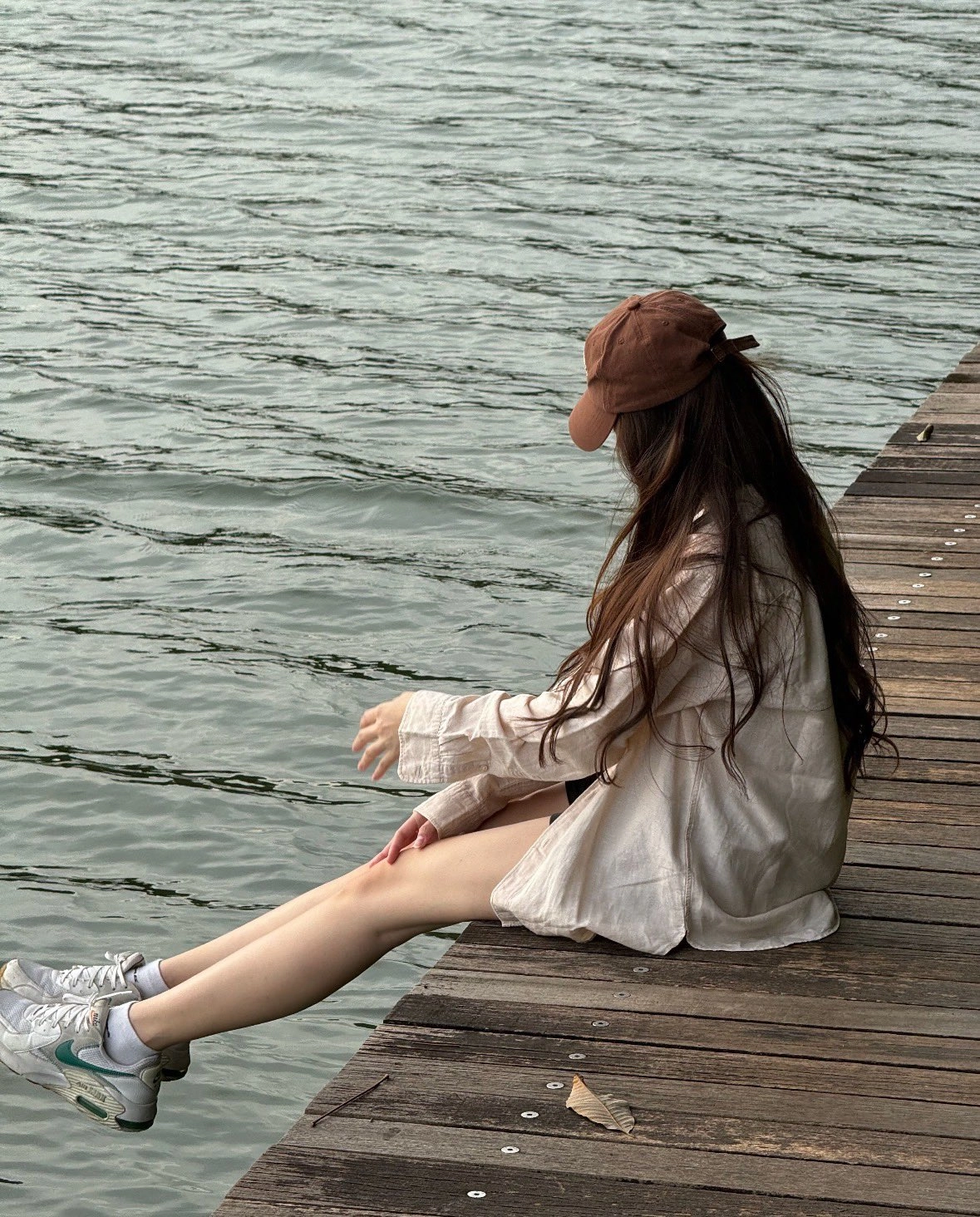 穿着棕色帽子的女人坐在一个码头上。