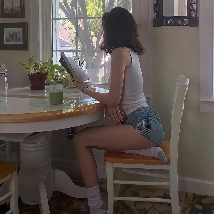 女人坐在一张桌子上读一本书。