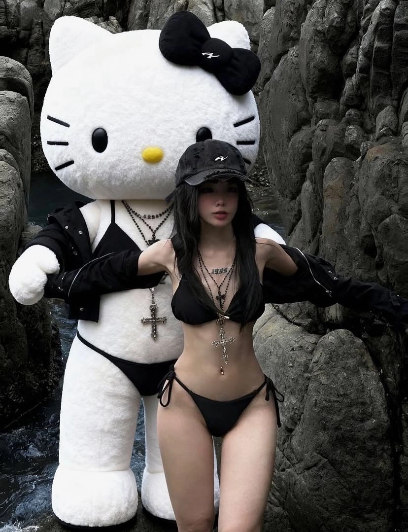 穿着比基尼的女人站在一个Hello Kitty娃娃旁边。