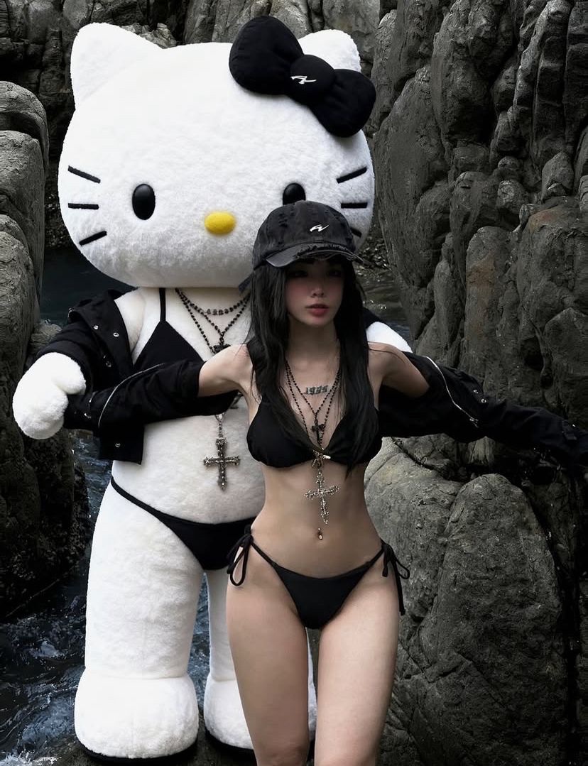 穿着比基尼的女人站在一个Hello Kitty娃娃旁边。