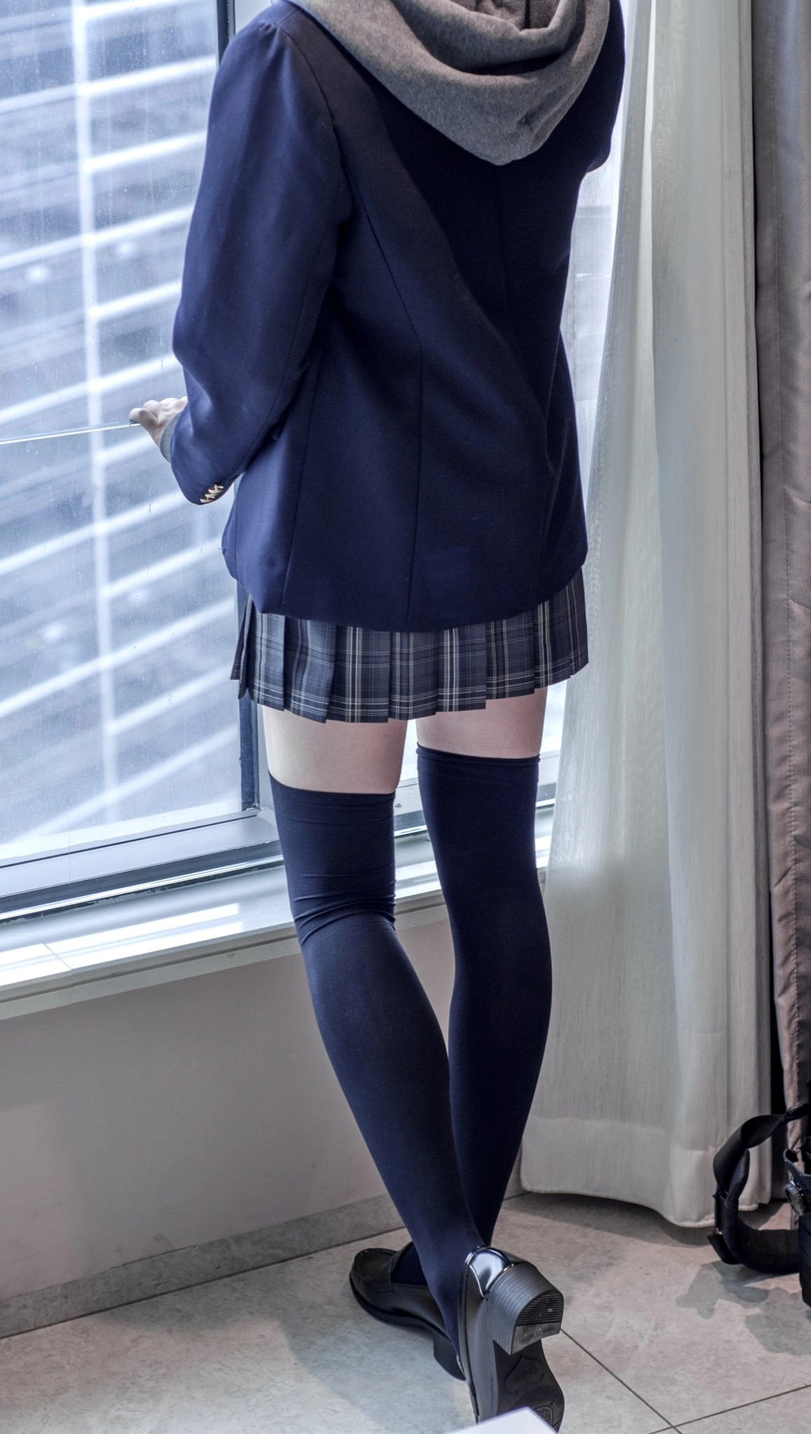 穿着蓝色夹克和一个的裙子的女人站在窗口。