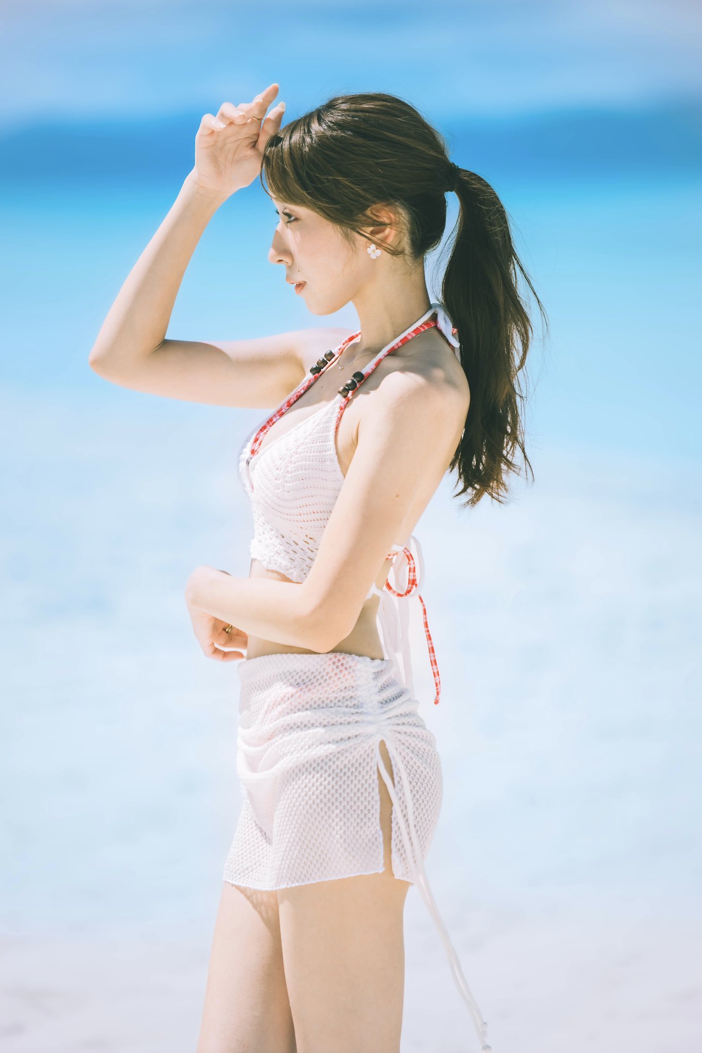 穿着白色裙子和红色领带的女人站在海滩上。