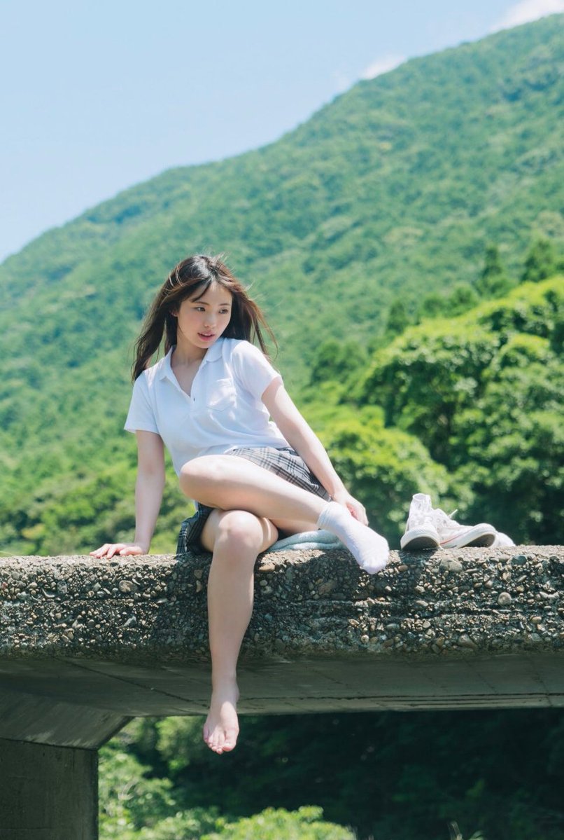 穿着白色衬衫和裙子的女人坐在岩石上。