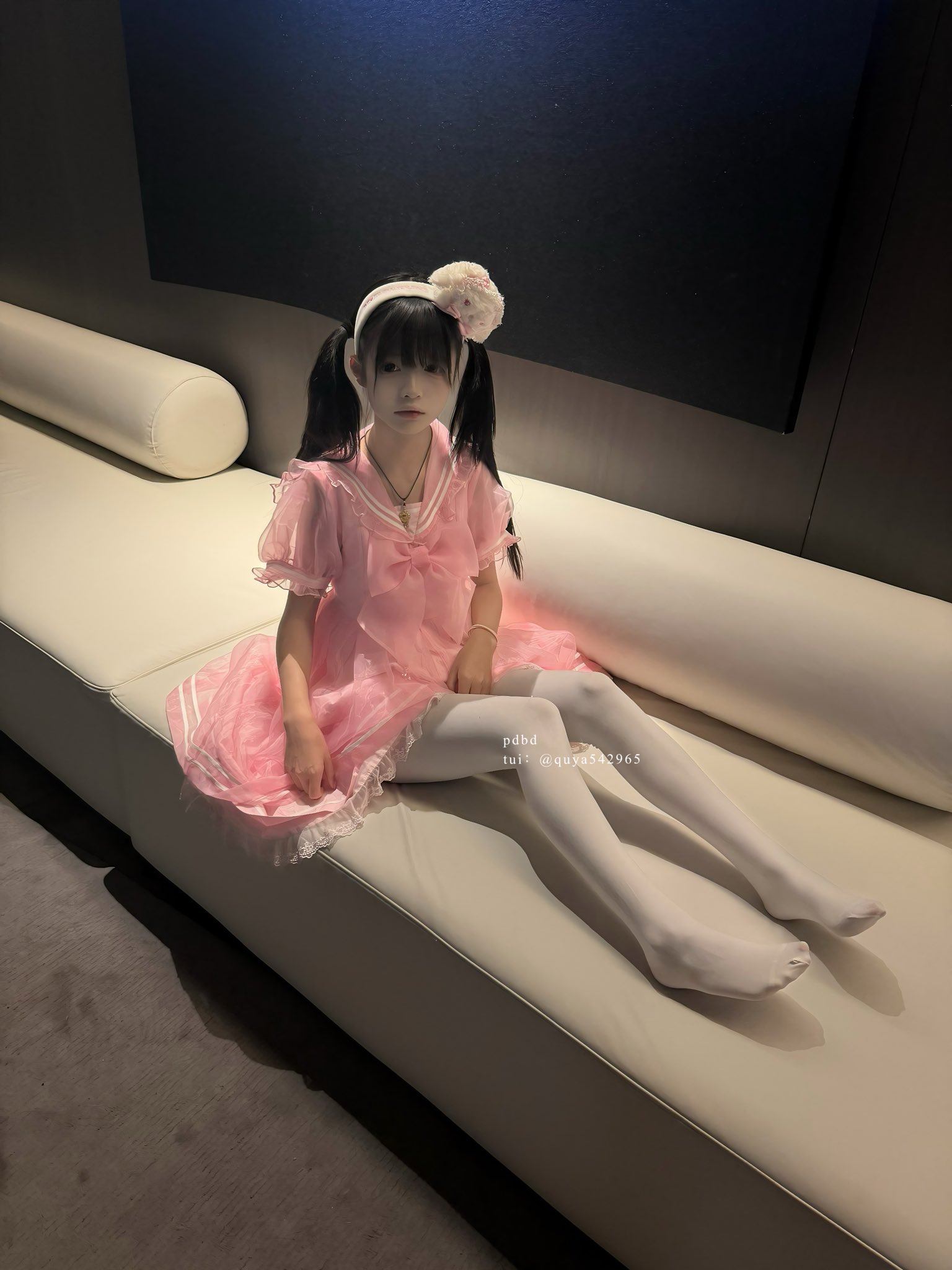 一位穿着粉红色的裙子和白色裤子的年轻女孩坐在沙发上。