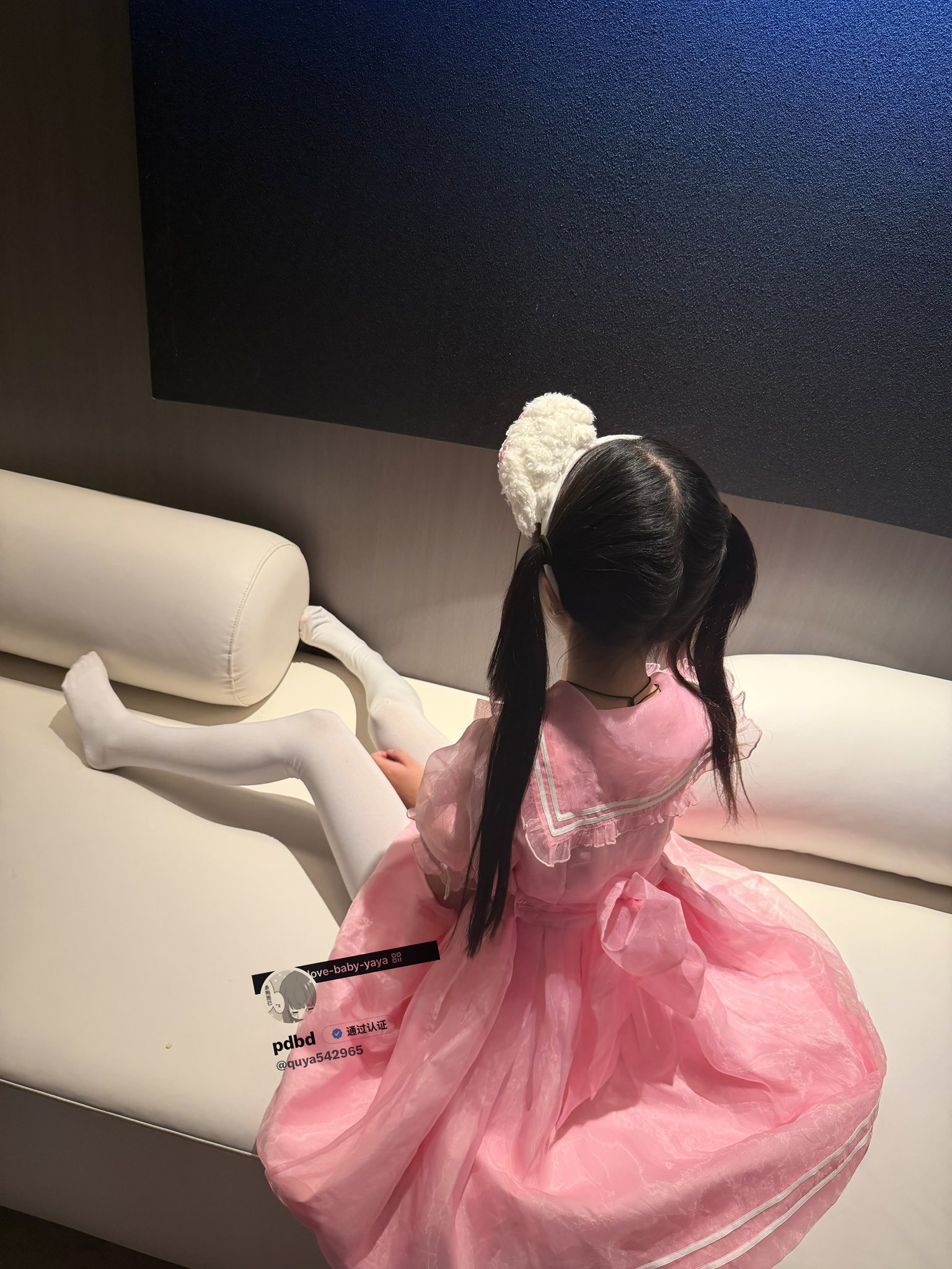 一位穿着粉红色的裙子和白色裤子的年轻女孩坐在沙发上。