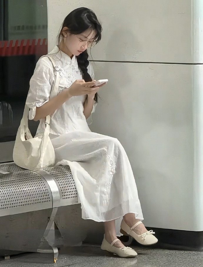 穿着白色衣服的女人坐在一个凳子上,看着她的手机。