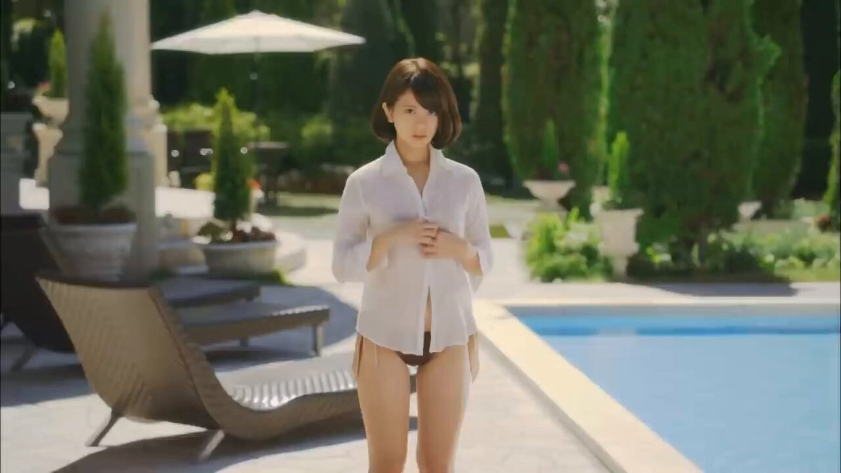 一位穿着白色衬衫和内衣的女人站在游泳池前面。