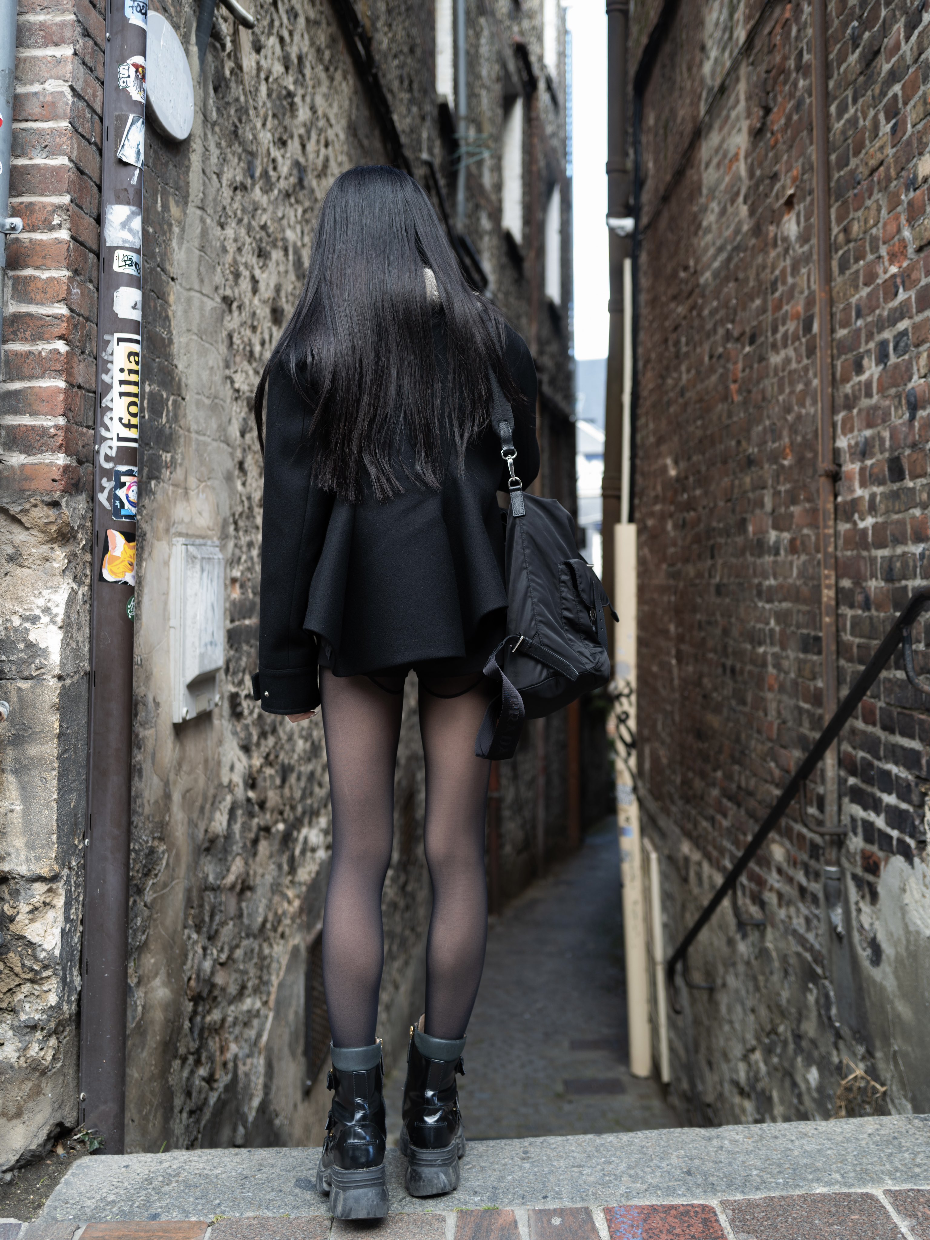 长头发和黑色衣服的女人走在一个狭窄的街道上。