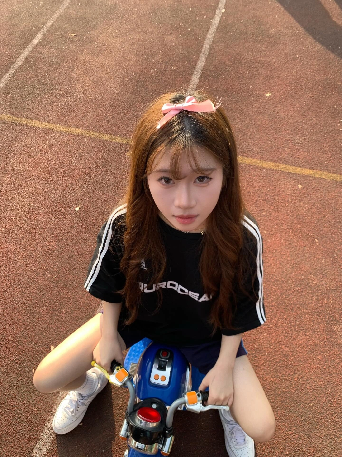 穿着黑色衬衫和粉红色的弓的女孩坐在摩托车上。