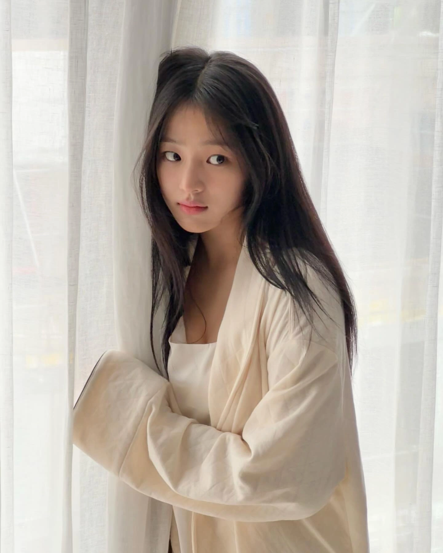 长头发和白色外套的女人站在窗前。