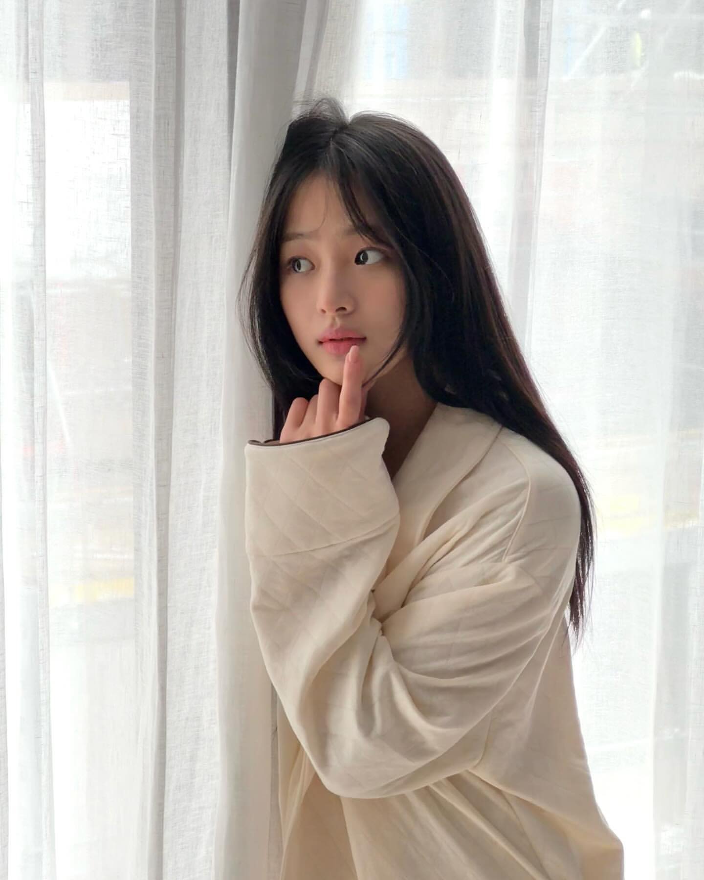 长头发和白色外套的女人站在窗前。