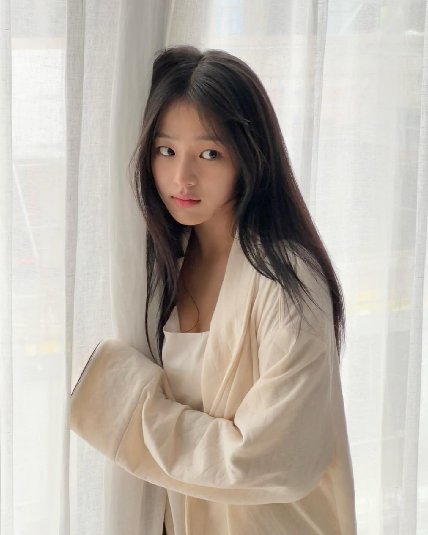 长头发和白色外套的女人站在窗前。