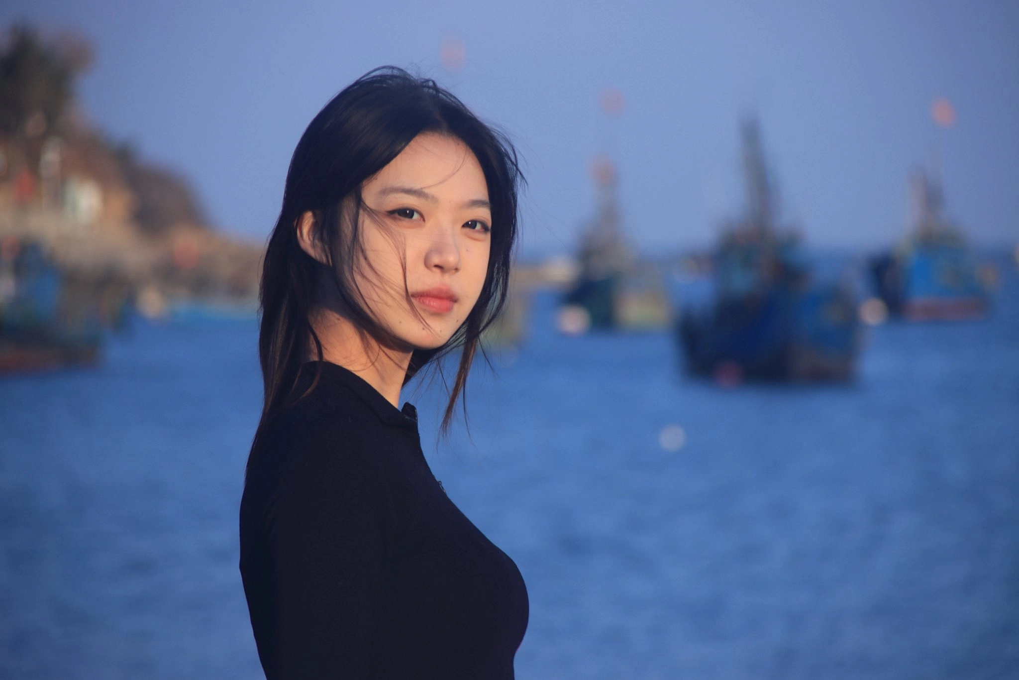 长头发和黑衬衫的女人站在海滩上。