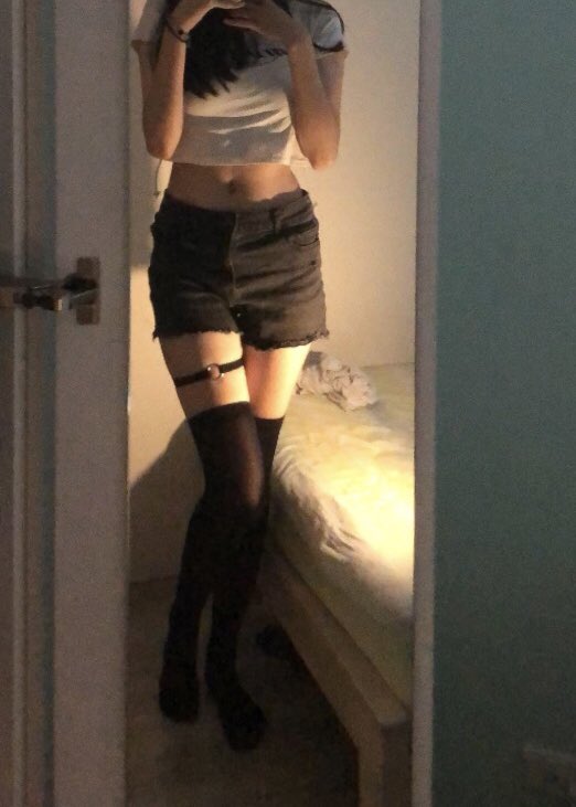 一位穿着白色衬衫和黑色短裤的女人在镜子前拍自拍。