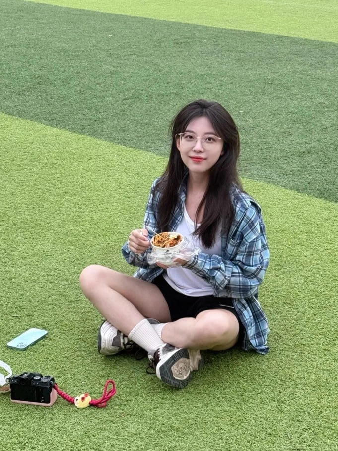 穿着的衬衫的女人坐在草地上吃饭。