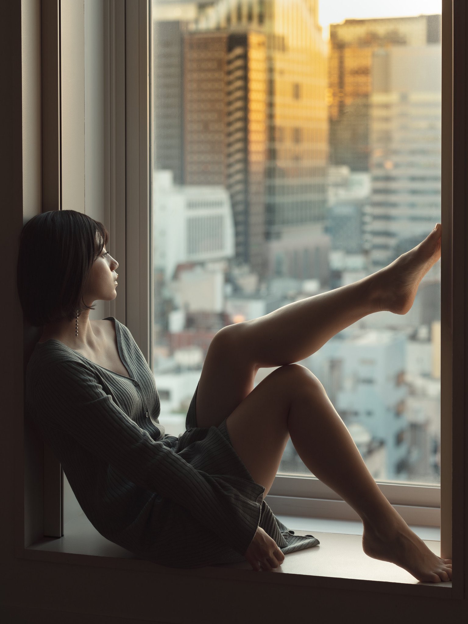 一位穿着灰色衣服的女人坐在窗户上,望着城市。