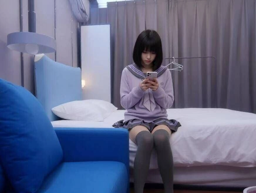 穿紫色衬衫的女人坐在床上,看着她的手机。