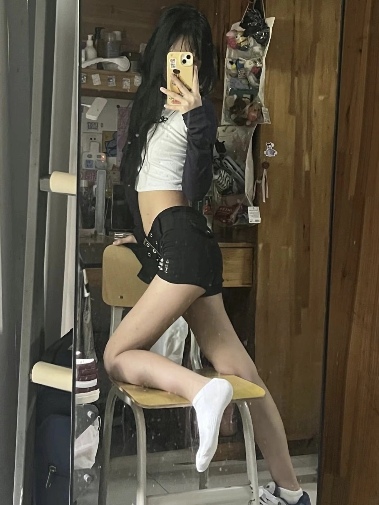 一位穿着白色衬衫和黑色短裤的女人在镜子前拍自拍。