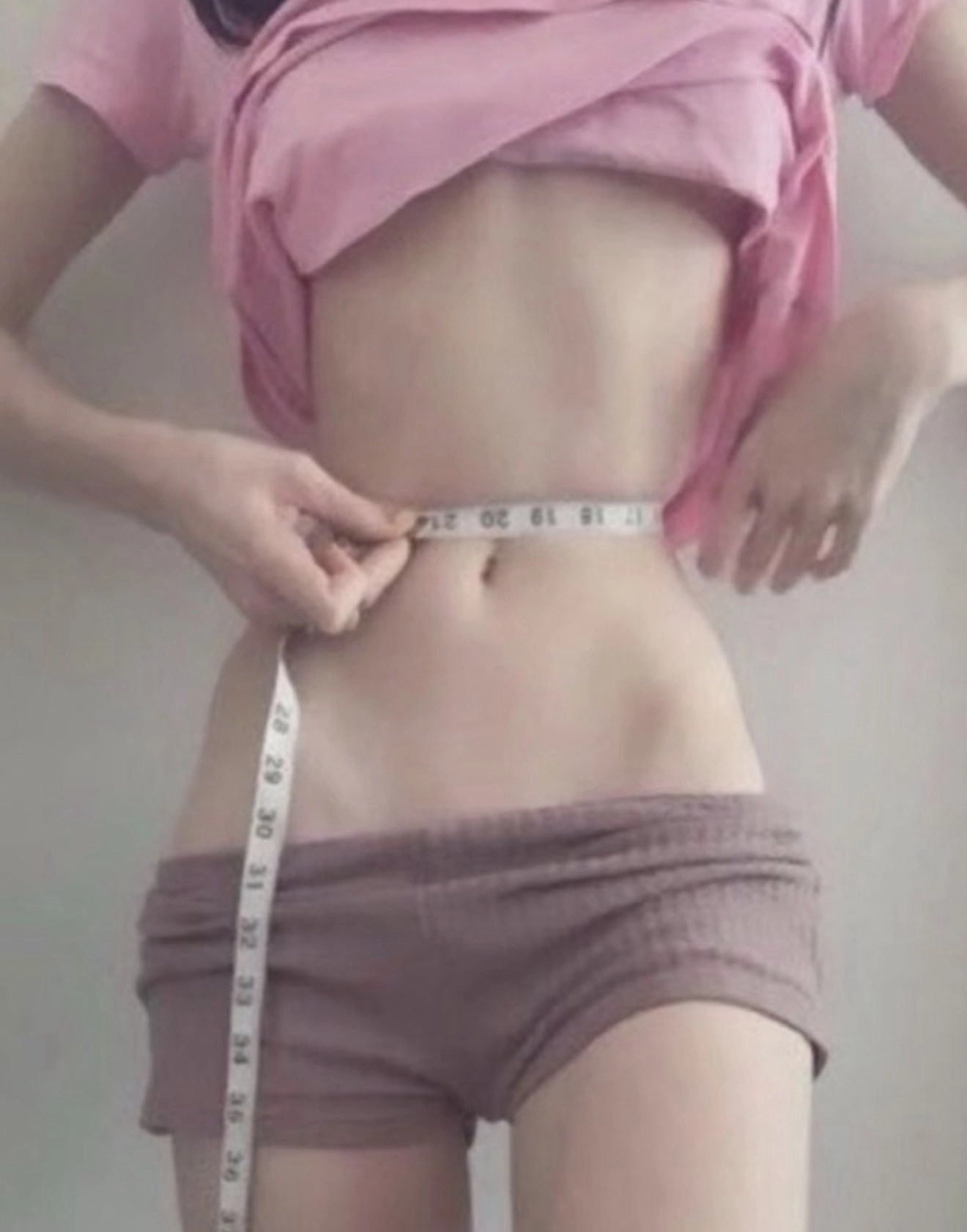 穿着粉红色的衬衫和短裤的女人握着一个胶带尺寸。