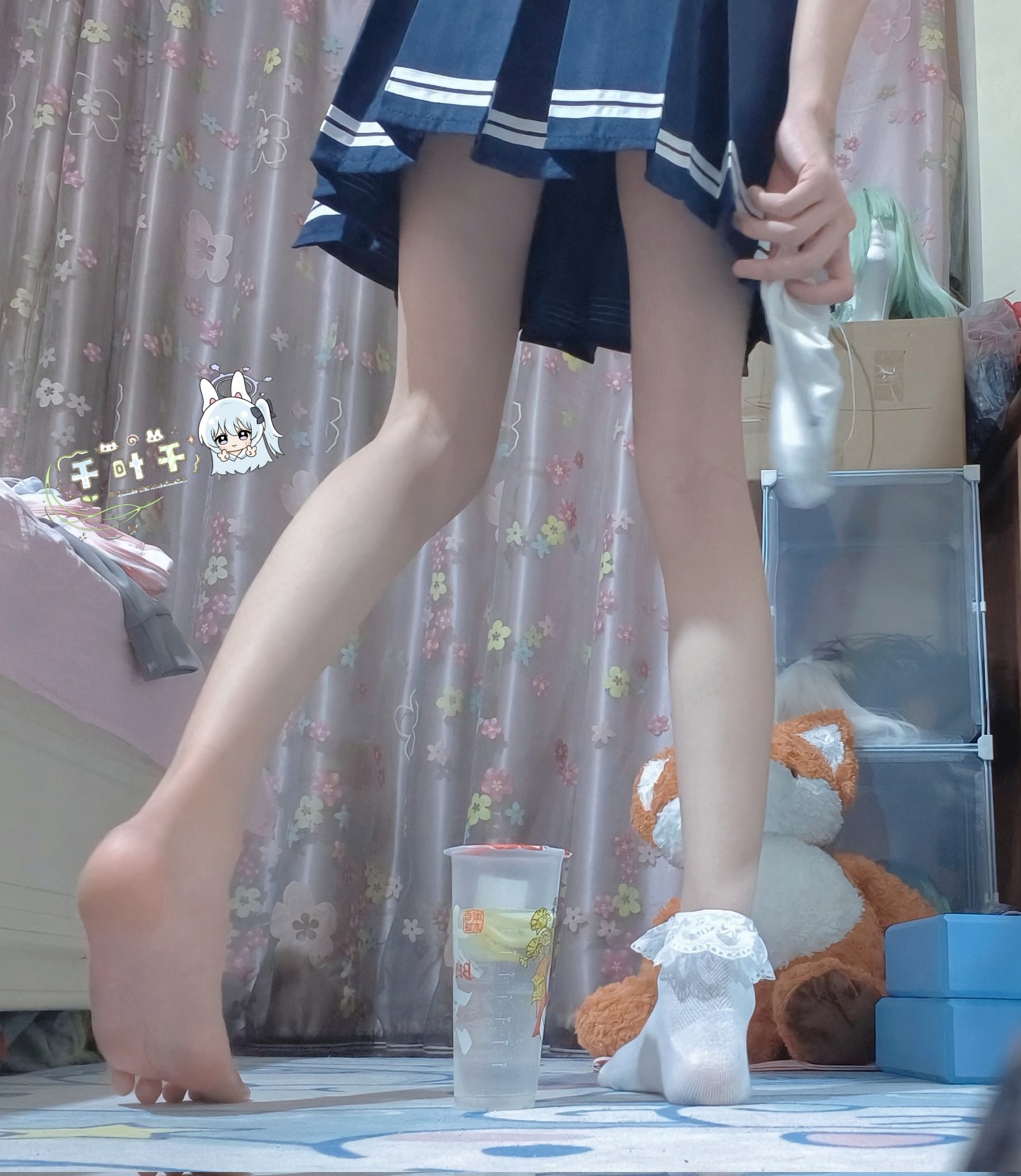 一位穿着蓝色衣服的女孩站在一间房间里,带着一只被填满的动物和一杯。