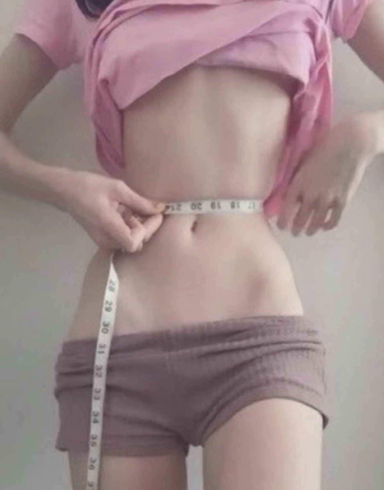 穿着粉红色的衬衫和短裤的女人握着一个胶带尺寸。