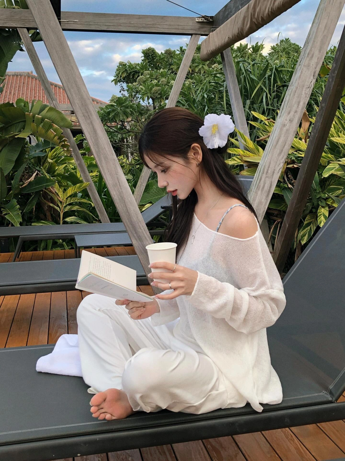 一位穿白衣的女人坐在休息椅上读一本书。