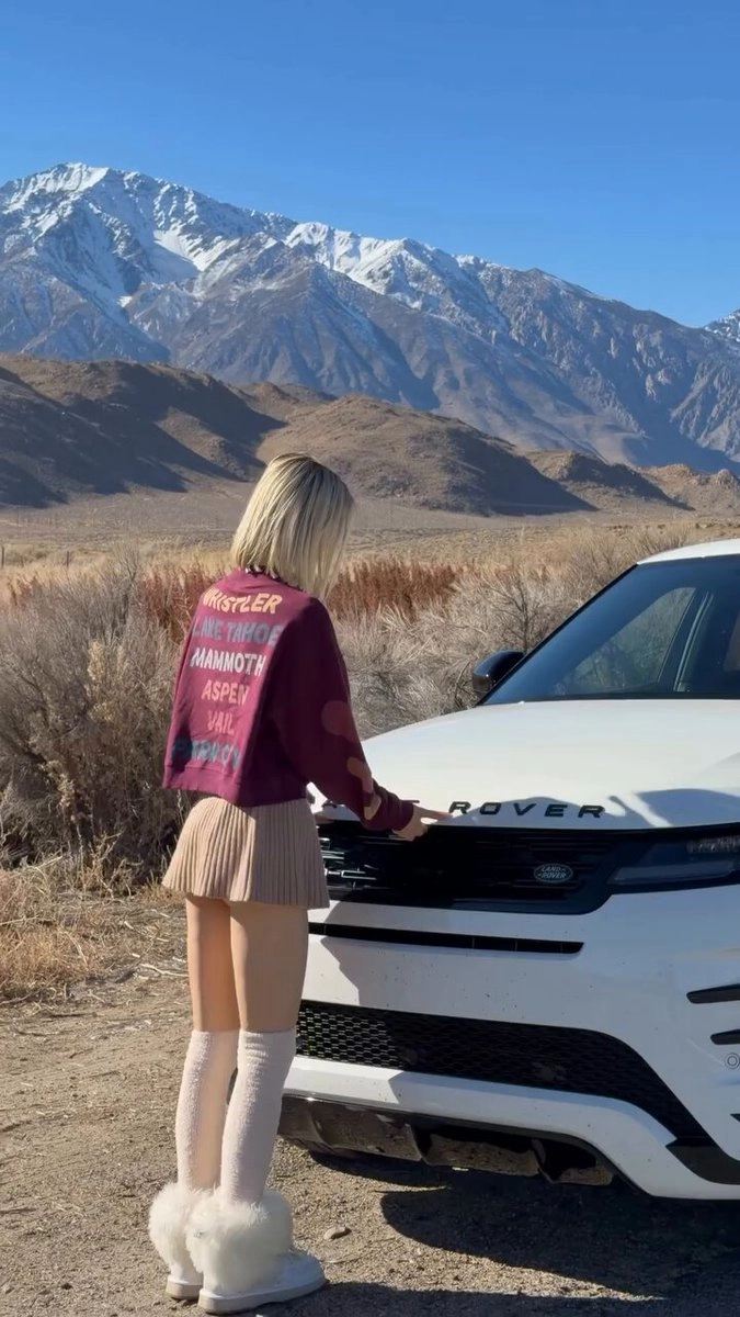 穿红色夹克的女人站在一辆白色车旁边。