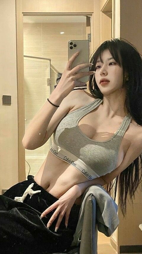 一位穿着灰色坦克顶和黑色裤子的女人在镜子前拍自拍。