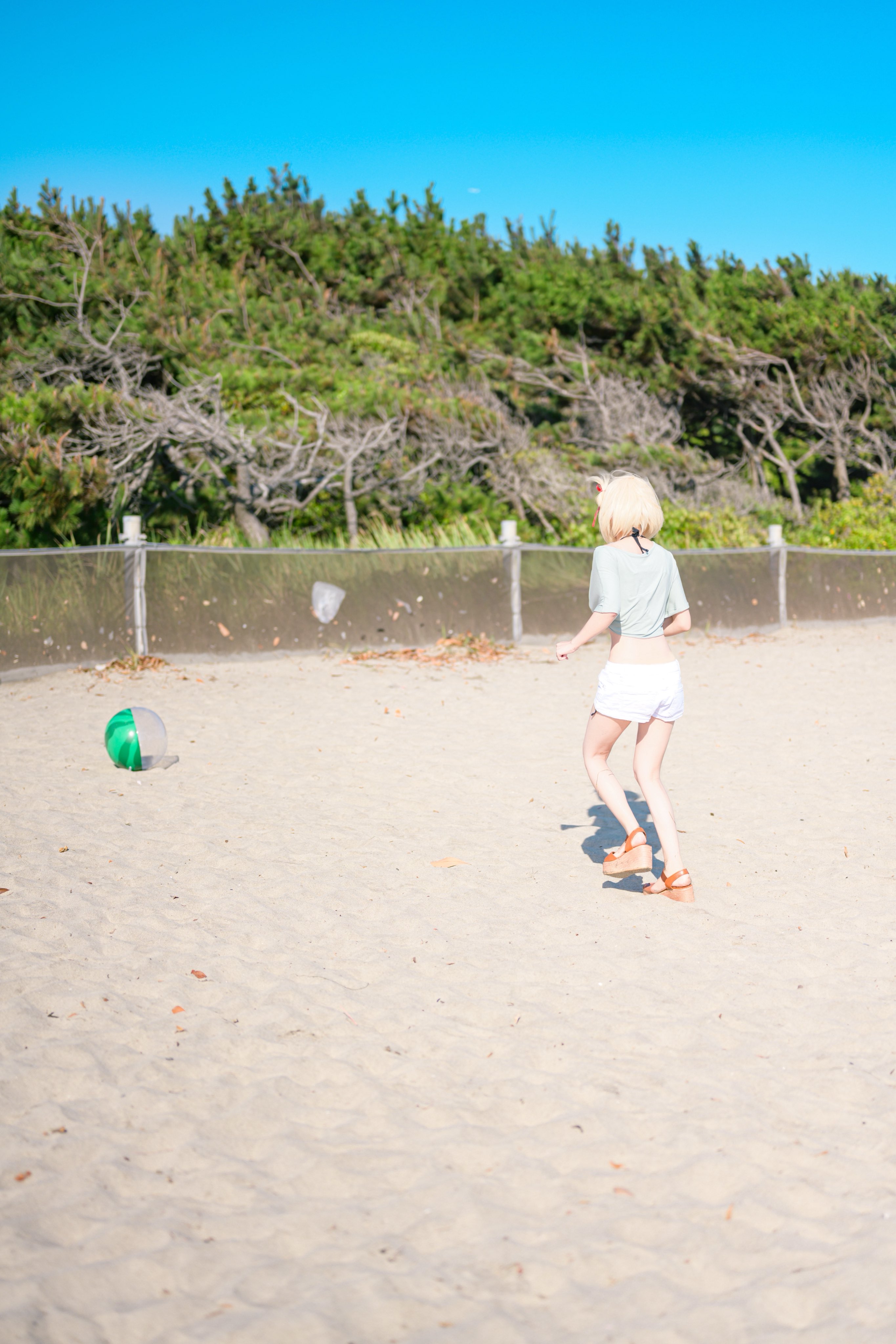 一位穿着绿色衬衫的女人在沙滩上和弗里斯比玩耍。