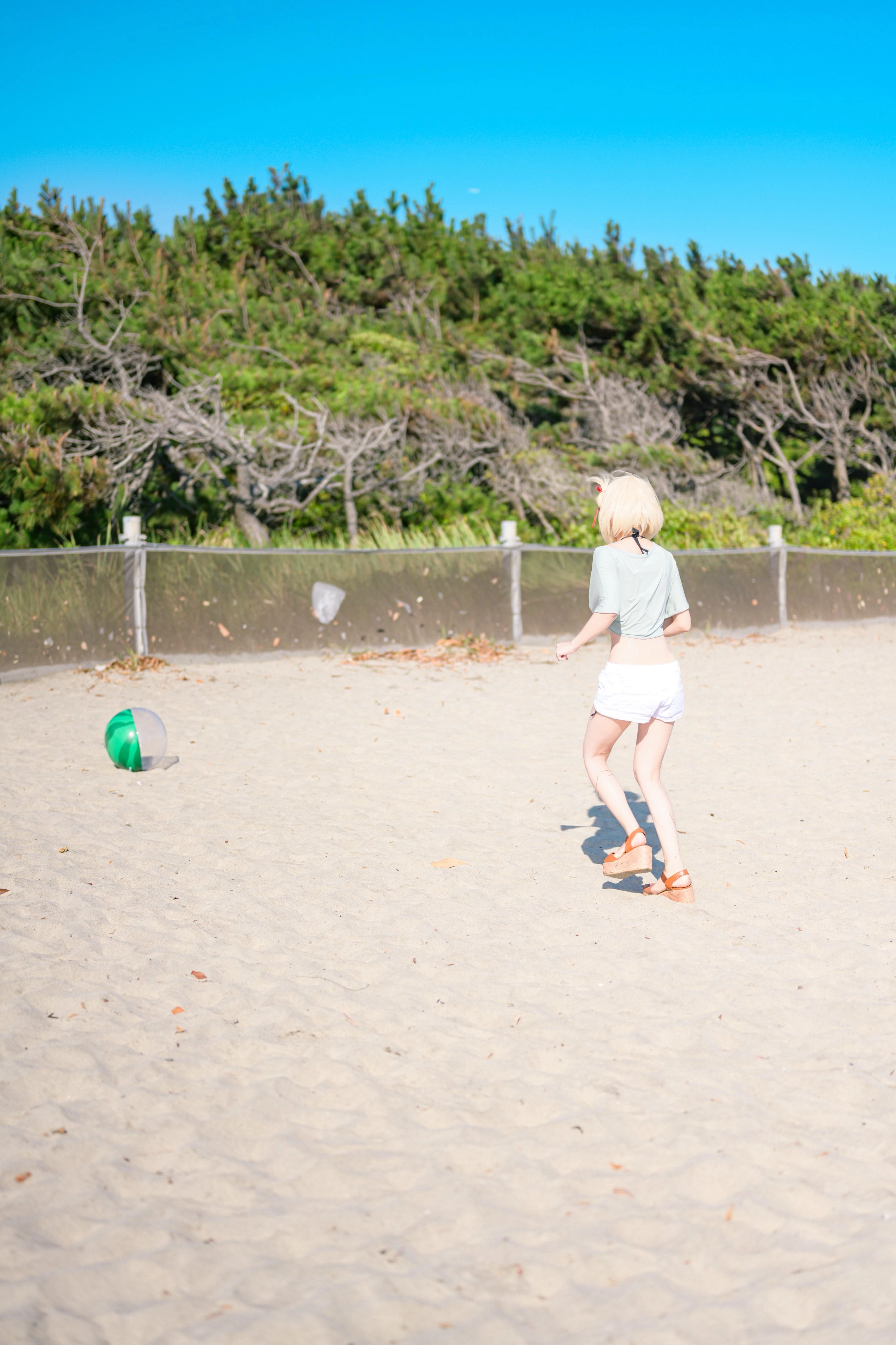 一位穿着绿色衬衫的女人在沙滩上和弗里斯比玩耍。