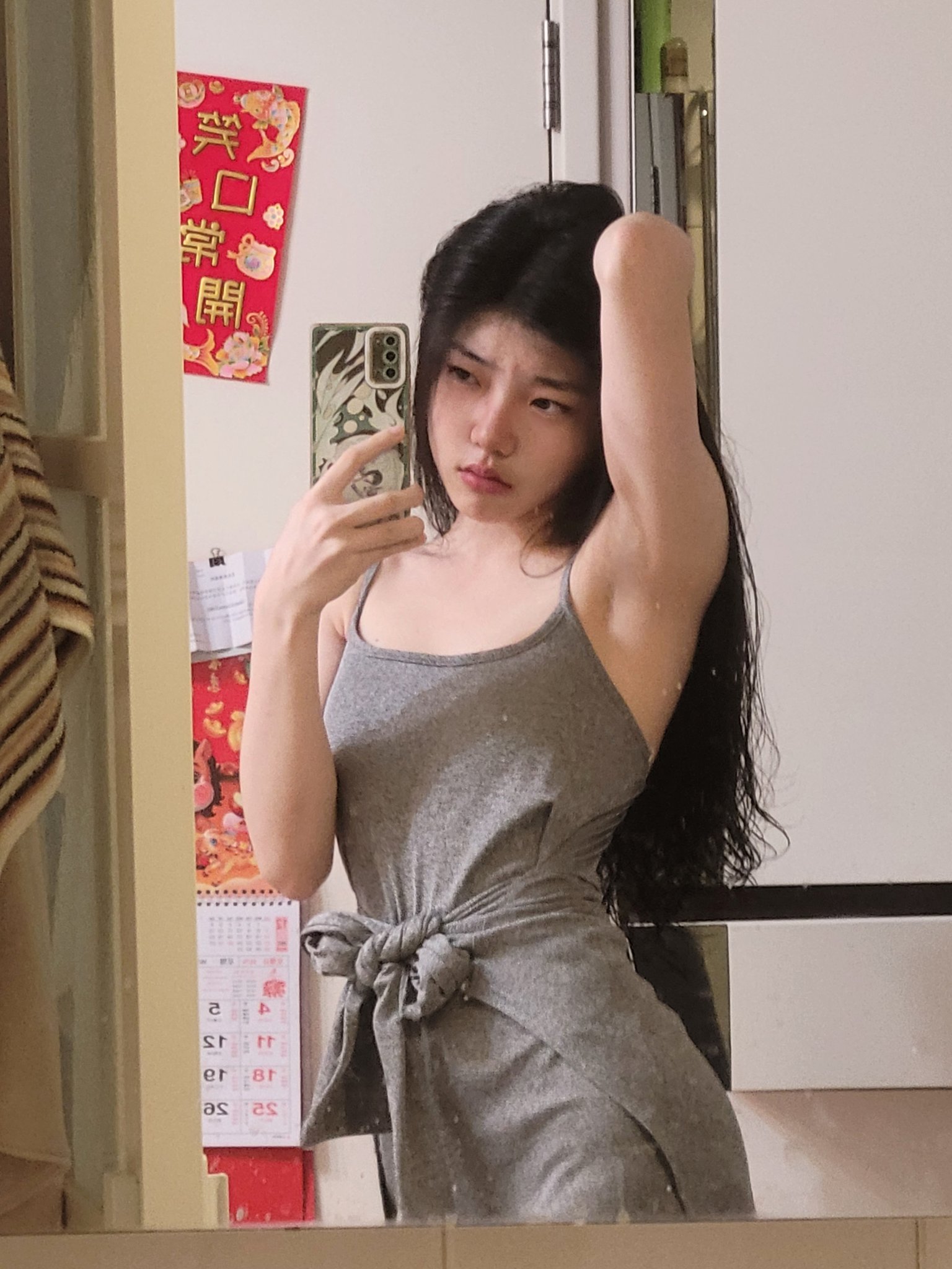 一位穿着灰色坦克顶的女人在镜子前拍自拍。