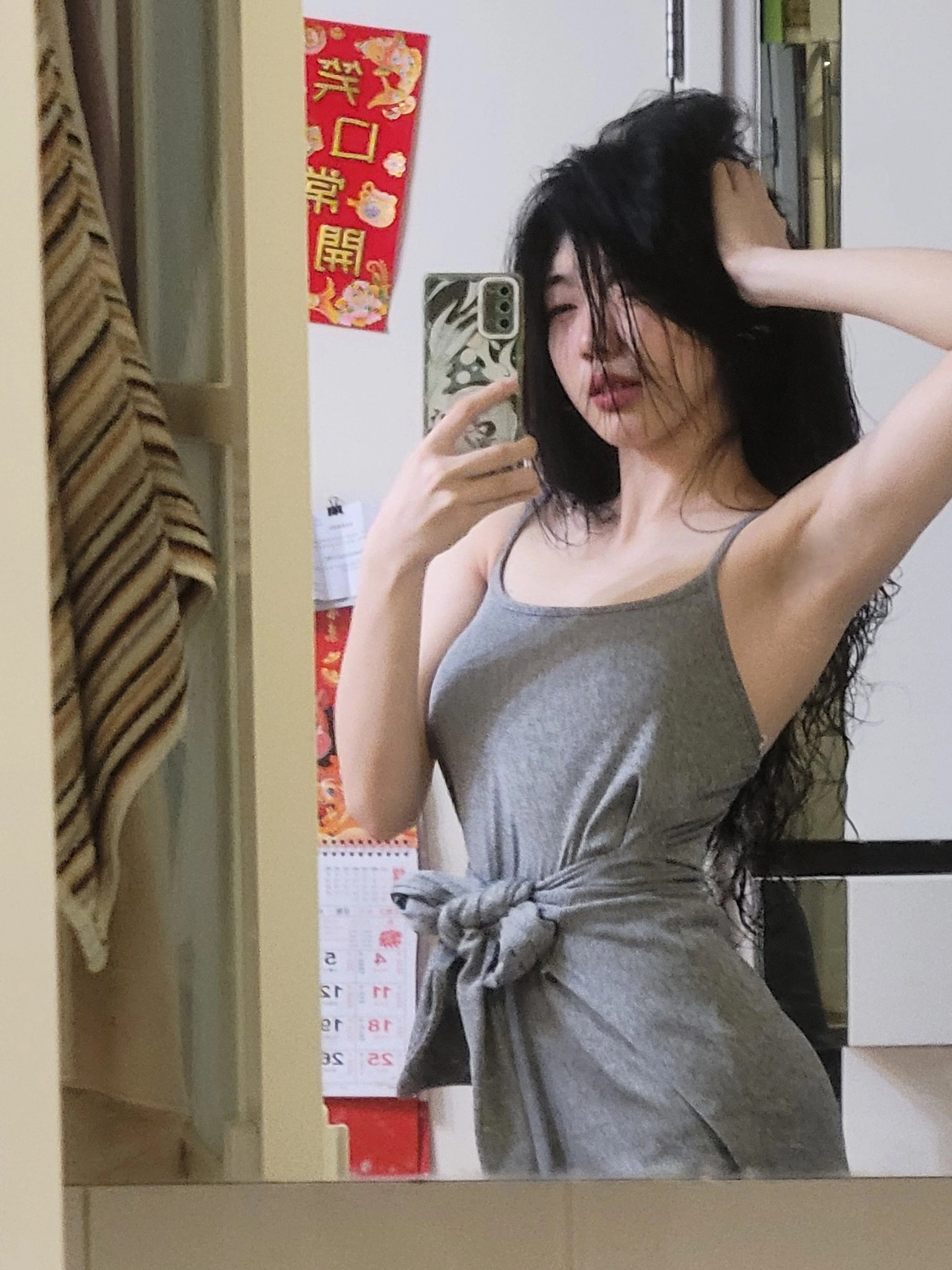 一位穿着灰色坦克顶的女人在镜子前拍自拍。