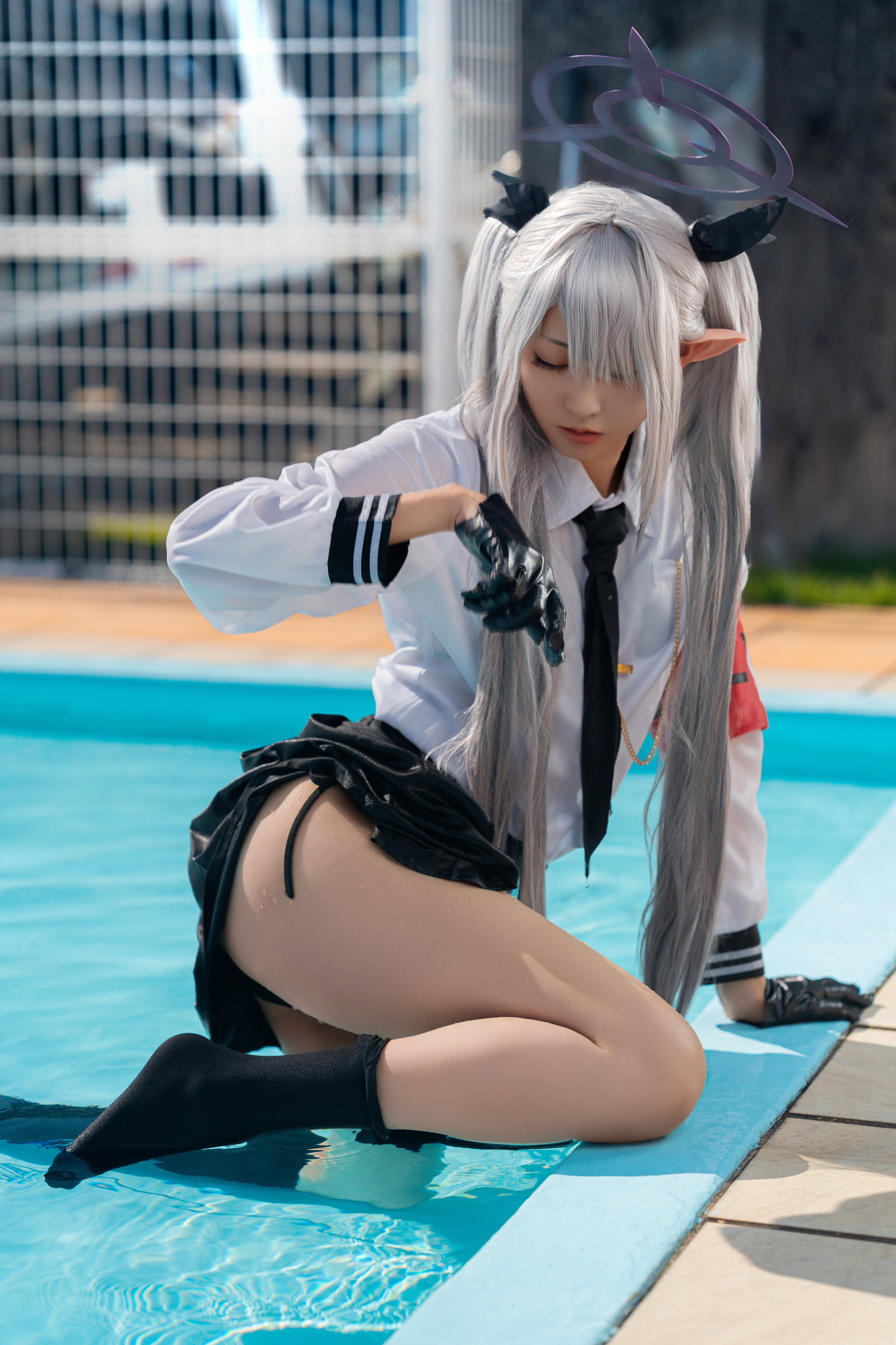 一位穿着白色衬衫和黑色领带的女人坐在游泳池旁。