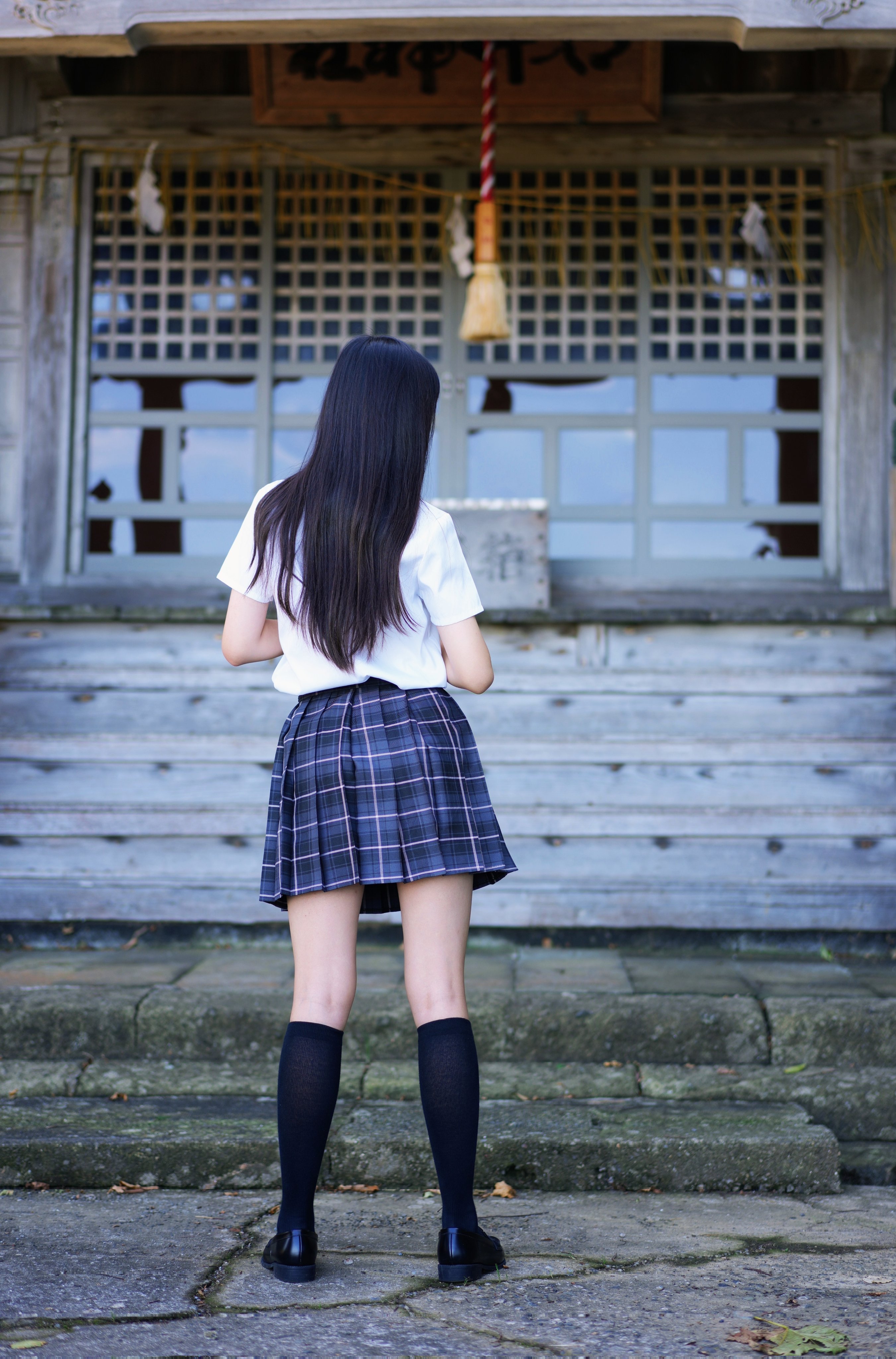 穿着白色衬衫和蓝色裙子的女孩站在阳台上。