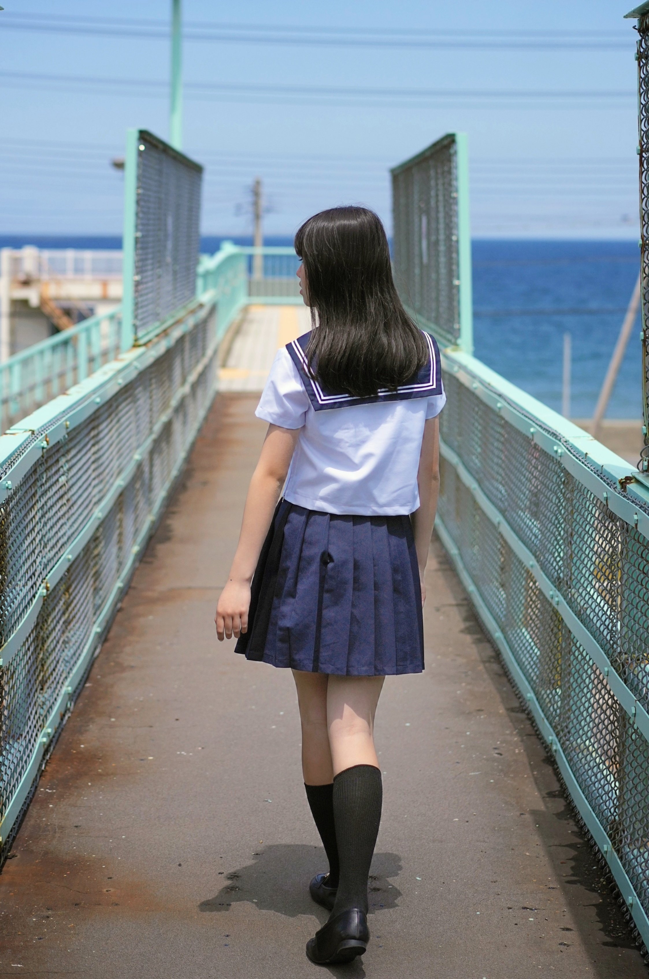 穿着白色衬衫和蓝色裙子的女孩站在阳台上。