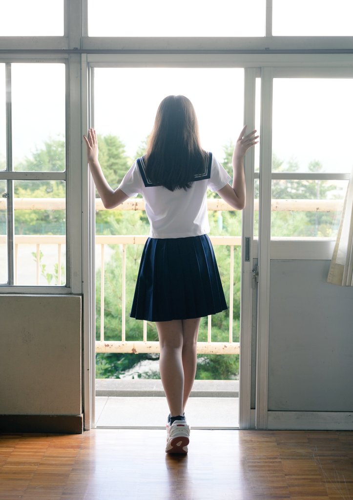 穿着白色衬衫和蓝色裙子的女孩站在阳台上。