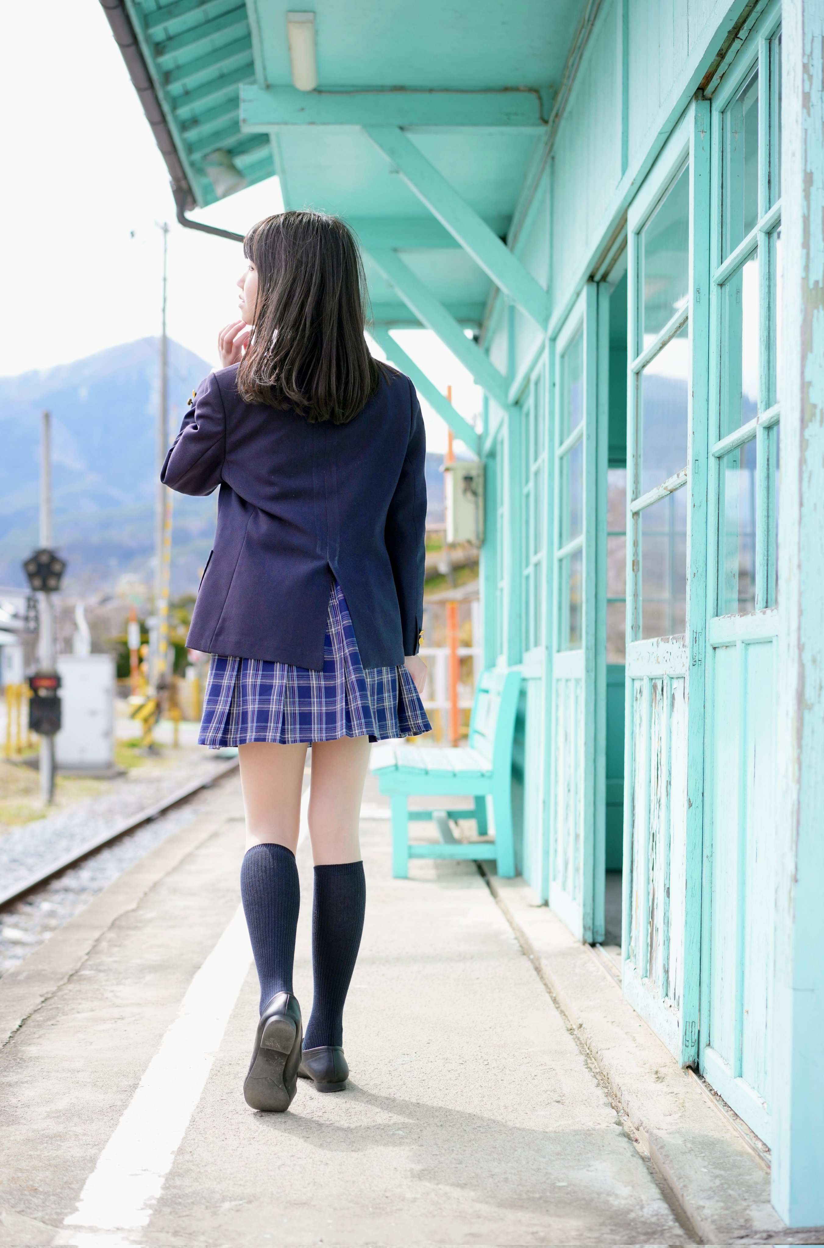 穿着白色衬衫和蓝色裙子的女孩站在阳台上。