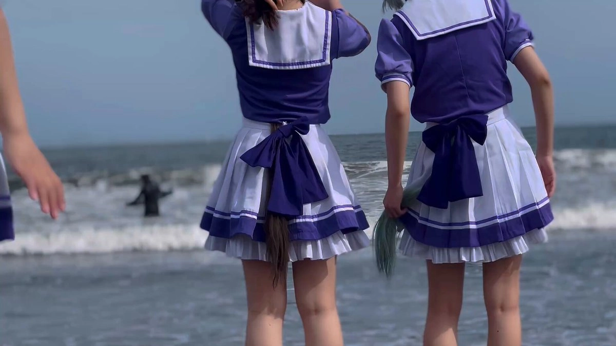 两个长发和蓝色裙子的女孩站在海滩上。