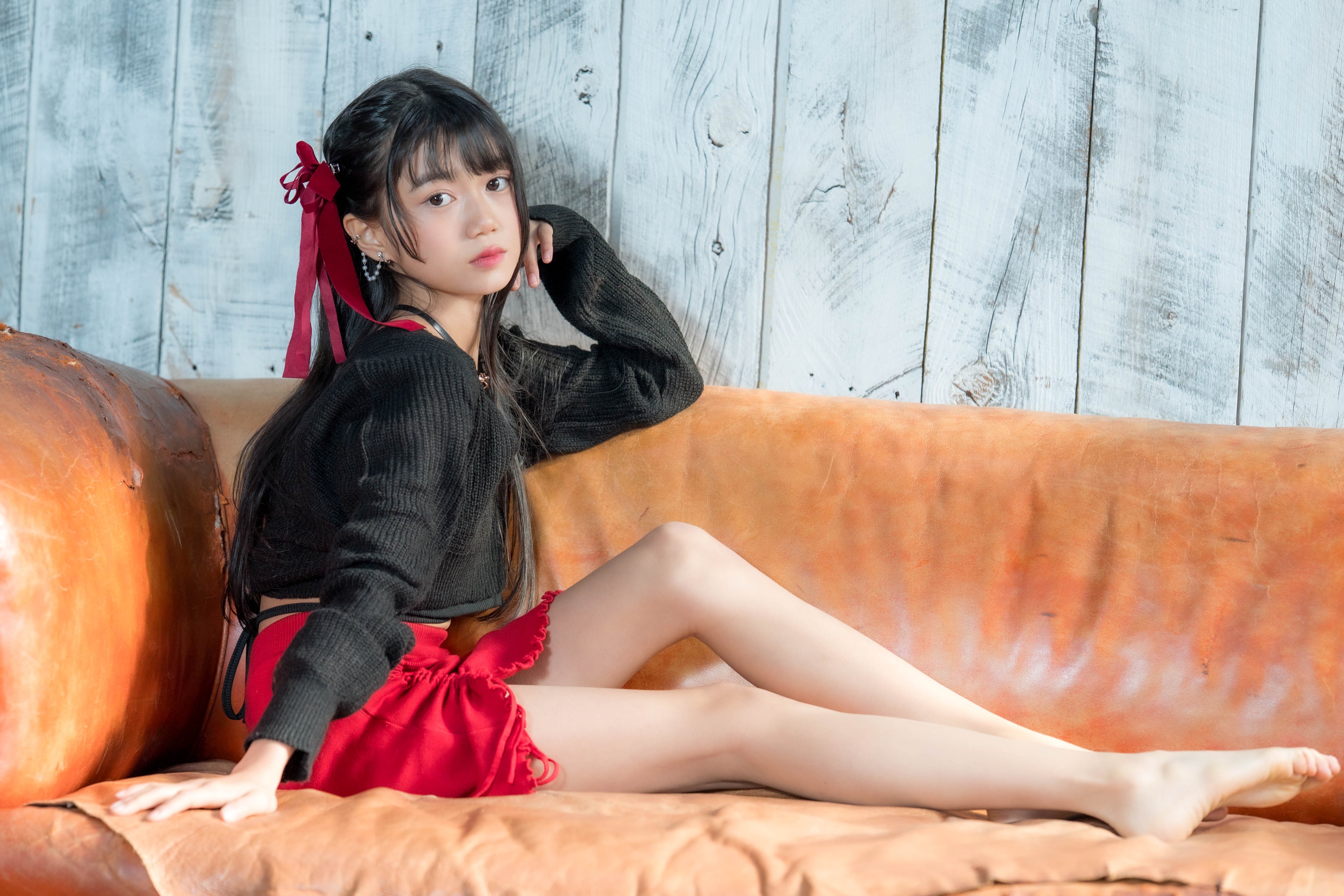 穿着黑色衬衫和红色裙子的女孩坐在沙发上。