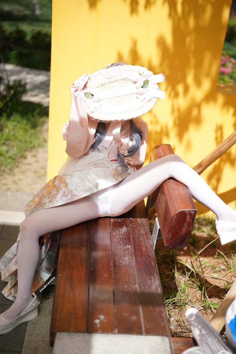 穿着粉红色的裙子和一顶白色的帽子的女人坐在一个凳子上。